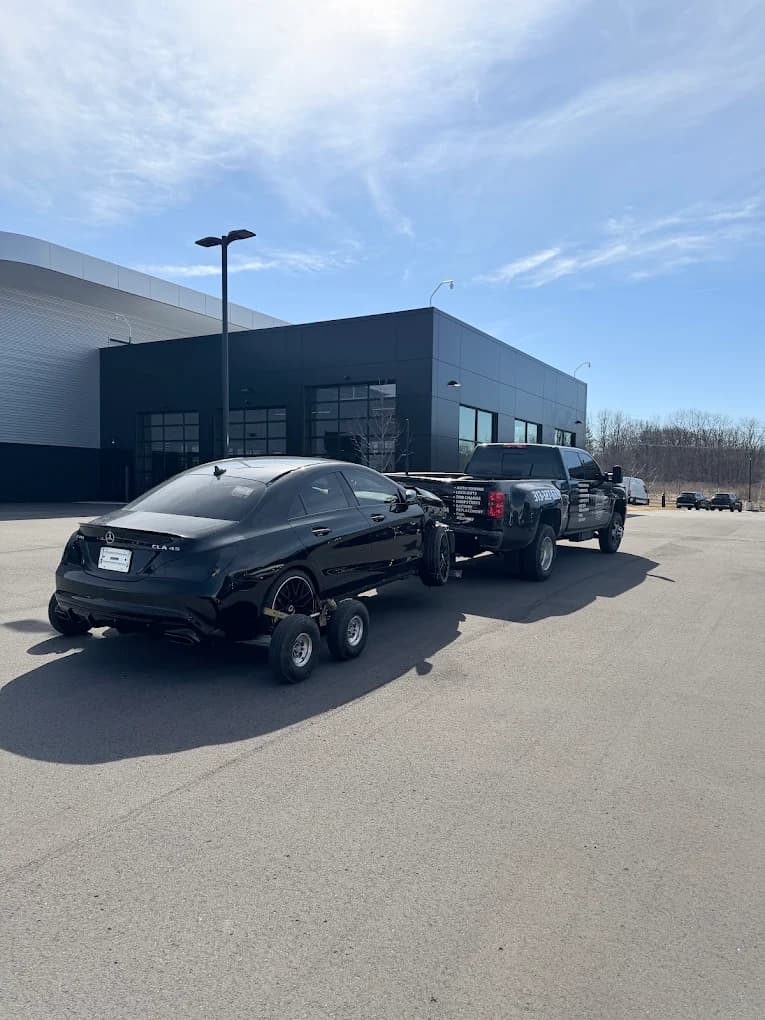 Prime O Towing flatbed Silverado transporting a black Mercedes CLA 35 AMG from a Metro Detroit dealership lot